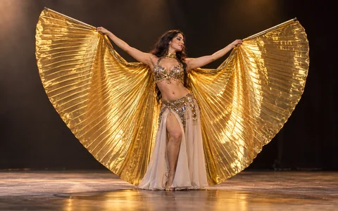 Danseuse adulte sur scène avec de grandes ailes d’Isis dorées ouvertes, photographie réaliste